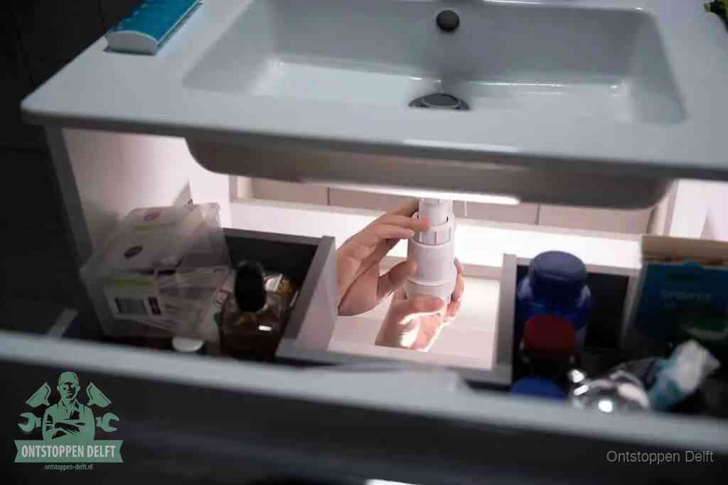 Een pompfles met zeep boven een wastafel, de heet water en afwasmiddel-methode om een vetprop in de afvoer los te maken in Delft