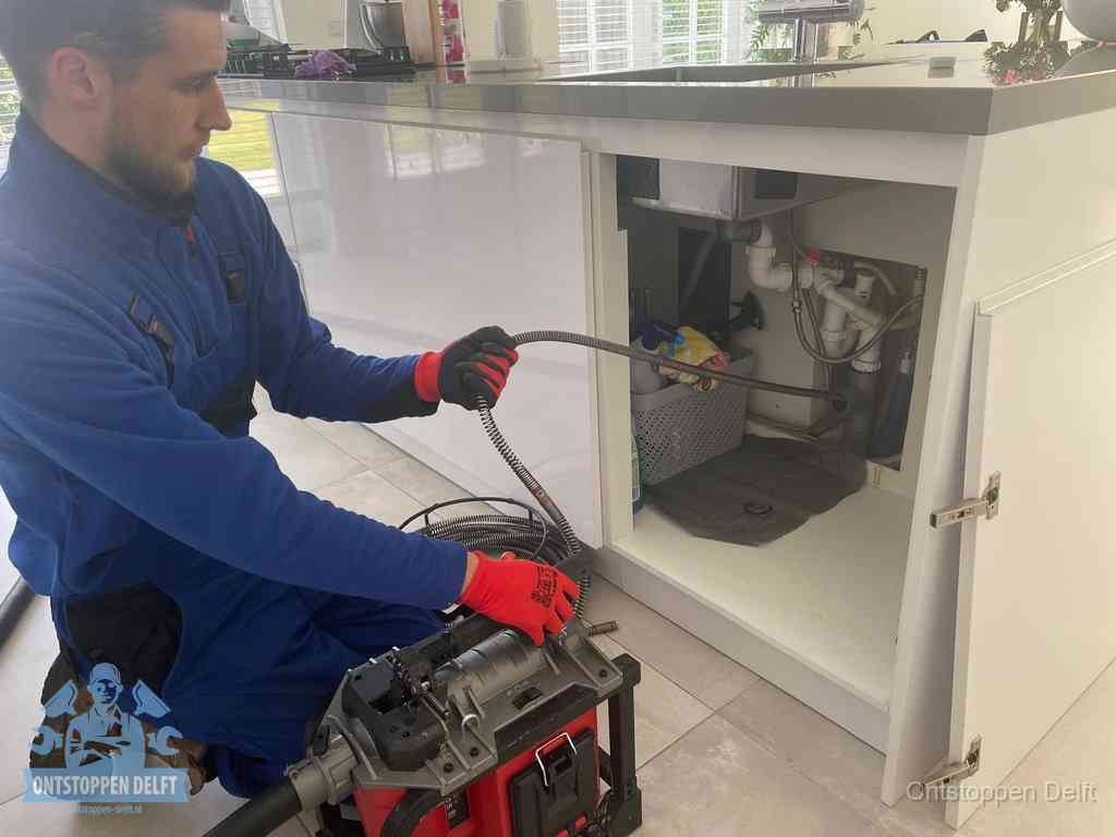Monteur voert een ontstoppingsveer in de afvoer onder de keuken in Delft