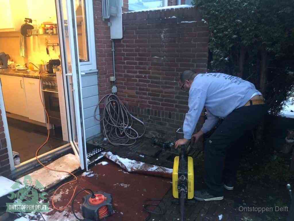 Een monteur werkt buiten bij een open riool-/grondput met een elektrische ontstoppingsmachine om een verborgen afvoerprobleem op te sporen in Delft