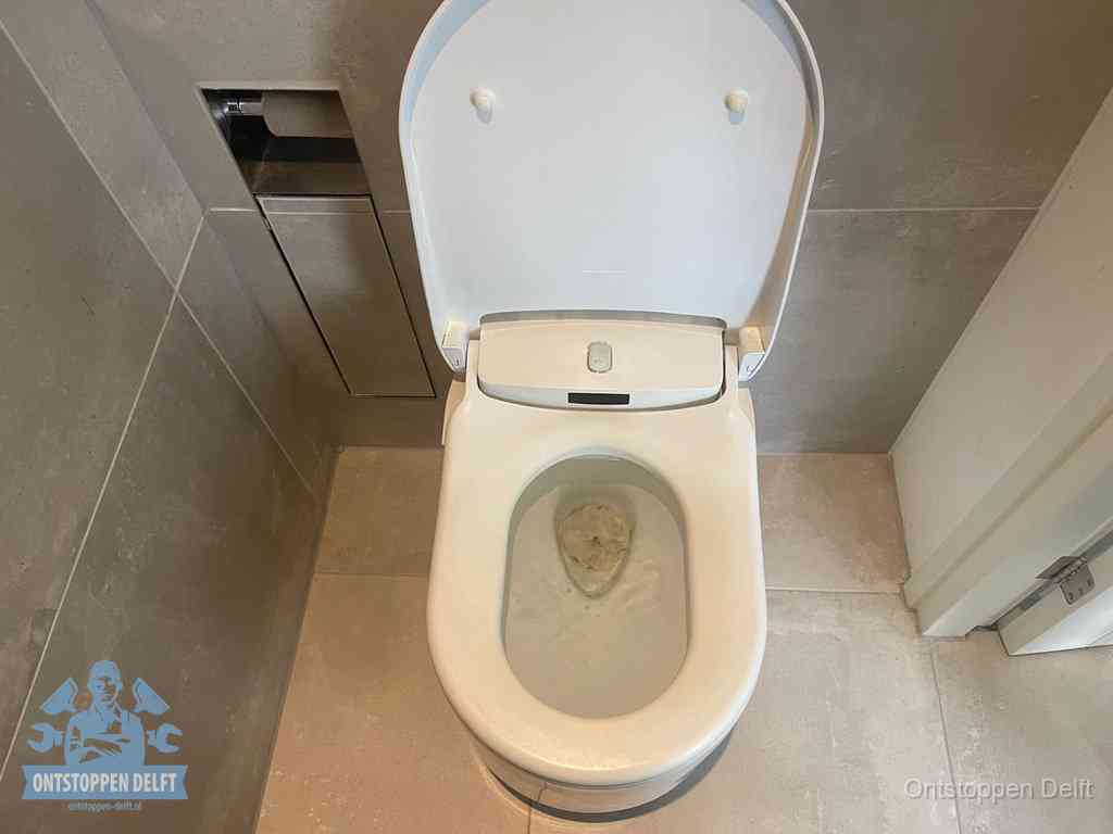 Een wit hangtoilet waarin een prop wc-papier op het water blijft drijven, een duidelijk signaal van een verstopte wc in Delft