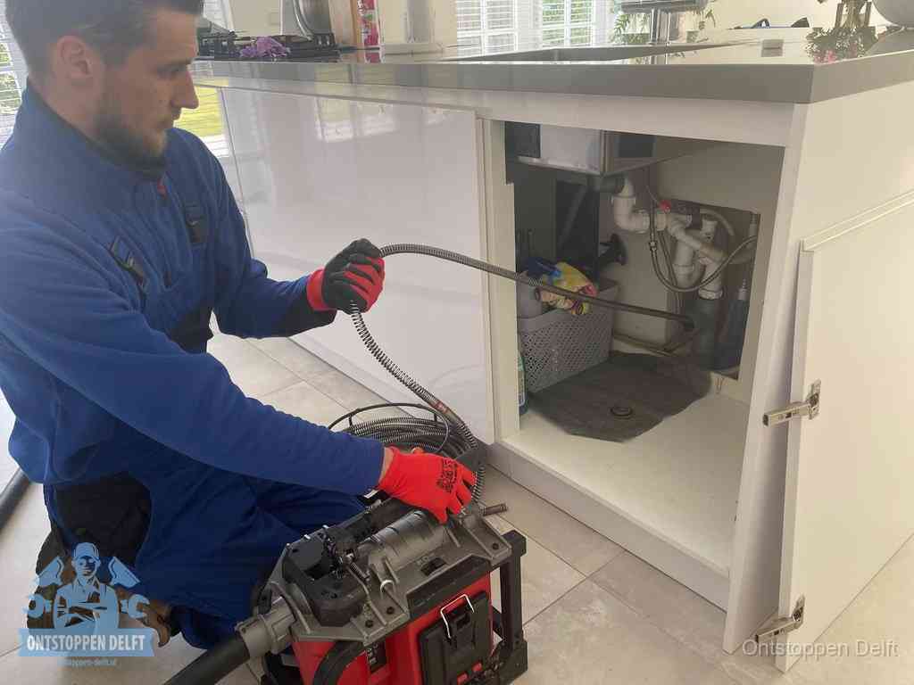 Een monteur reinigt de keukenafvoer grondig met een veermachine om terugkerende gootsteenverstoppingen te voorkomen in Delft