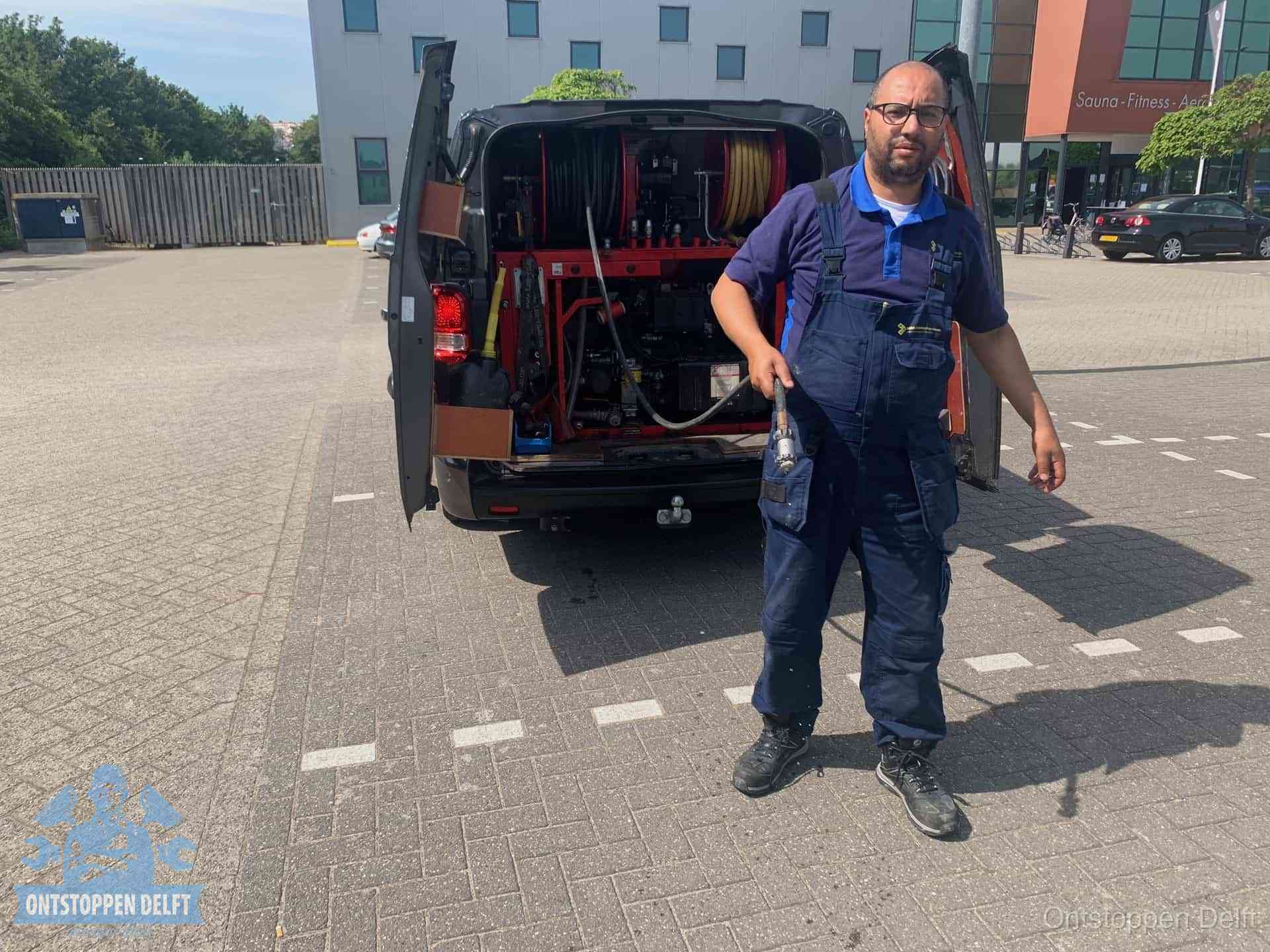 Een monteur bij zijn bestelbus met een hogedruk- en rioolreinigingsunit, klaar om de oorzaak van terugkerende wc-verstoppingen aan te pakken in Delft