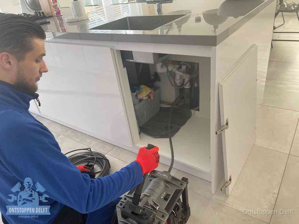 Monteur ontstopt met een veermachine een verstopte afvoer onder de gootsteen in Delft