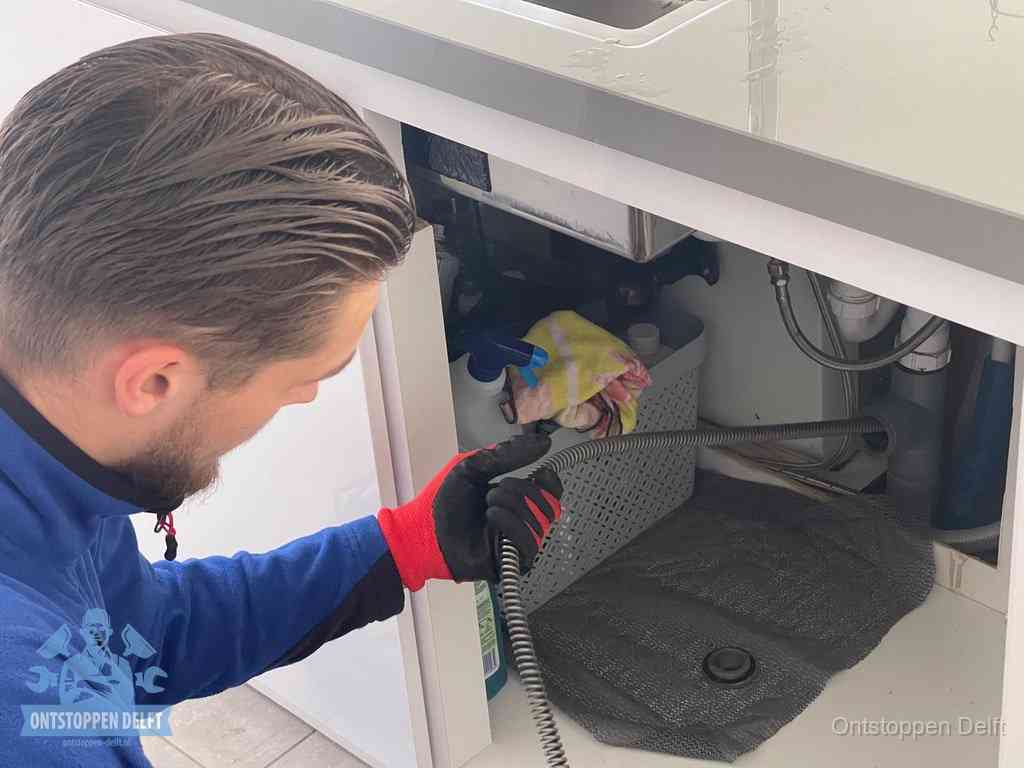 Een monteur voert een flexibele ontstoppingsveer in de afvoer om een verstopping voorbij de bocht van het toilet te bereiken in Delft
