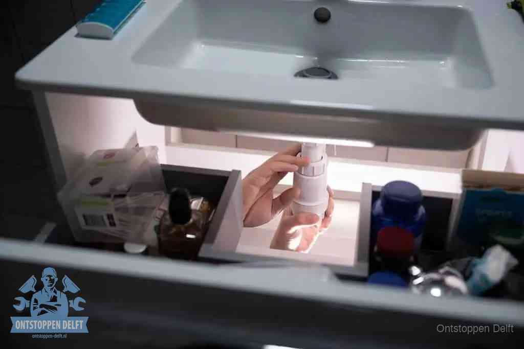 Een pompfles met zeep boven een wastafel in de toiletruimte, de warm water en afwasmiddel-methode om de wc te ontstoppen in Delft