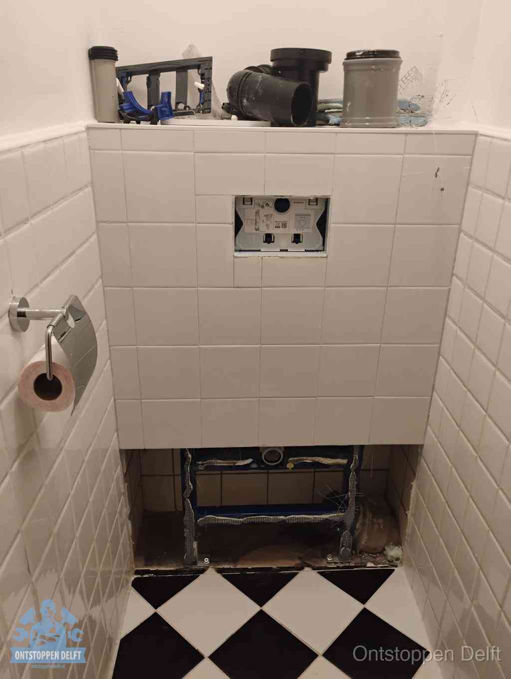 Een toiletruimte waar het hangtoilet en de inbouwreservoir-onderdelen zijn vrijgelegd voor onderhoud, periodiek nazicht voorkomt een wc-verstopping in Delft